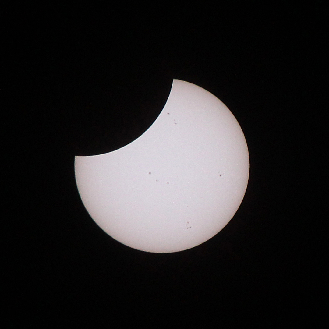 El Sol parcialmente eclipsado, fotografiado a través de un objetivo telefoto equipado con un filtro solar de uso específico. La Luna cubre el 30% del diámetro del Sol y aproximadamente el 19% de su superficie. Manchas solares oscuras salpican el disco solar.