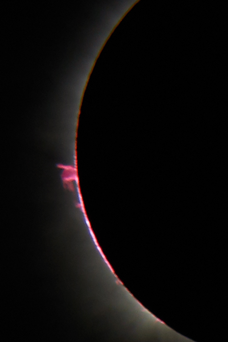 El inicio y el final de la totalidad ofrecen tus mejores oportunidades para examinar la delgada capa media de la atmósfera del Sol, llamada cromosfera. Esta brilla en la luz rojo rubí del hidrógeno gaseoso calentado a más de 20.000 °C (36.000 °F). También son visibles justo más allá de la silueta de la Luna las protuberancias solares: brillantes arcos rojos, bucles y chorros de gas caliente impulsados por la liberación explosiva de la energía magnética del Sol. Durante la totalidad, con la Luna cubriendo toda la brillante superficie del Sol, es perfectamente seguro observar el espectáculo sin filtros solares —de hecho, si intentas observar la totalidad con filtros solares, no verás nada en absoluto. Los prismáticos mostrarán especialmente bien la cromosfera y las protuberancias.